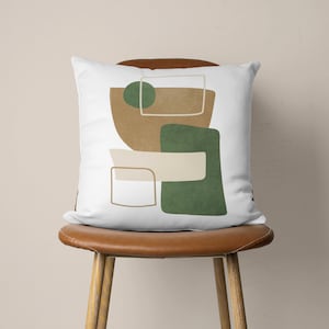 Puede incluir: Una almohada blanca con un dise&ntilde;o abstracto que presenta formas geom&eacute;tricas en tonos marrones y verdes.