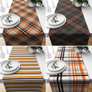 May include: Four different table runners with plaid patterns in various colours, including black, white, orange, and yellow. Each runner is laid out on a white surface with a plate and a small bouquet of flowers.