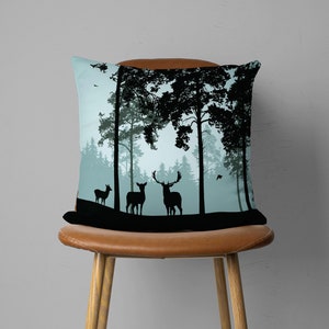 May include: A throw pillow with a blue and black design featuring a silhouette of a forest with deer. The deer are standing in a clearing in the forest. The pillow is on a brown chair.