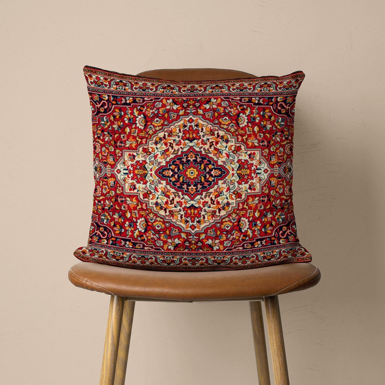 May include: A red, blue and white patterned throw pillow with a traditional Persian rug design. The pillow is sitting on a brown leather chair.