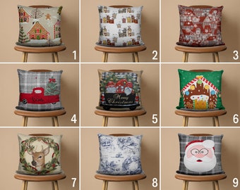 Pode incluir: Nove capas de almofada de Natal diferentes com vários designs, incluindo uma casa de gengibre, um caminhão vermelho, um veado e Papai Noel. As almofadas estão todas em cadeiras de madeira com um fundo bege.