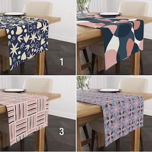 May include: Four different table runners with various geometric patterns. The table runners are on wooden tables with a light wood finish. The table runners are in the following order: 1. Navy blue with cream and white geometric shapes, 2. Navy blue with pink and white geometric shapes, 3. Pink and cream with black stripes, 4. Navy blue with pink and white floral pattern.
