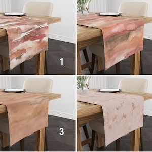 May include: Four different table runners with watercolour-style designs in shades of brown, pink, and orange. The runners are displayed on wooden tables with chairs.