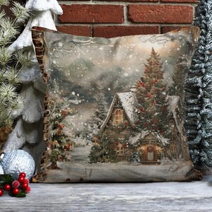 May include: A decorative throw pillow with a winter scene featuring a snow-covered cabin, a pine tree with red berries, and a snowy landscape. The pillow has a brown fabric with a distressed look and a zipper closure.