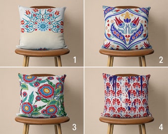 May include: Four decorative throw pillows with different patterns. The pillows are on brown chairs with wooden legs. The pillows are all square and have a white background. The first pillow has a blue and red floral pattern. The second pillow has a blue and red geometric pattern. The third pillow has a red and green floral pattern. The fourth pillow has a red and blue geometric pattern.