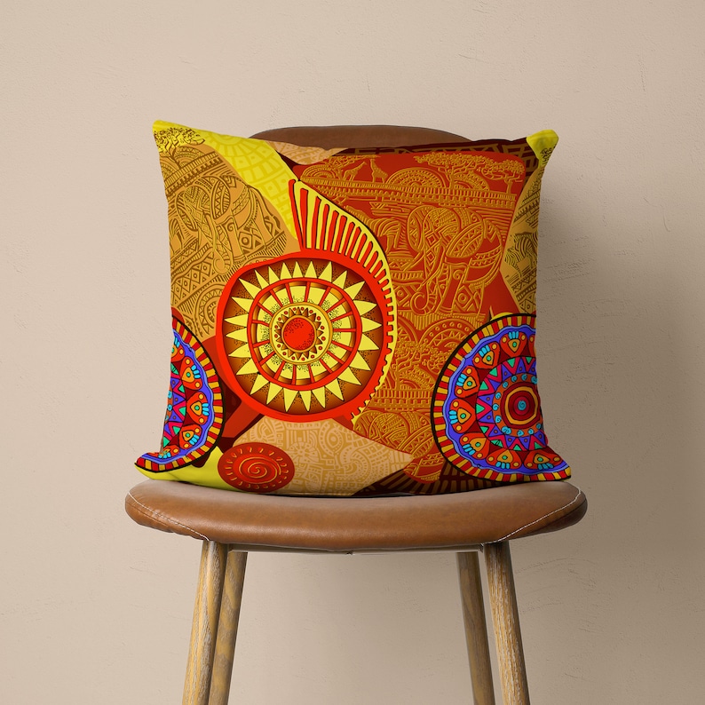Op de afbeelding: Een geel, rood en blauw kussen met een geometrisch patroon. Het kussen heeft een groot cirkelvormig patroon in het midden met kleinere cirkelvormige patronen eromheen.