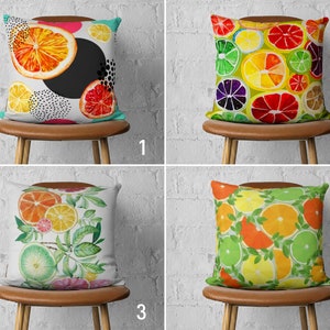 May include: Four decorative throw pillows with different citrus fruit designs. The pillows are on brown chairs with a white brick wall background. The pillows are all square and have a white background. The first pillow has a large orange slice in the center with smaller citrus slices and black polka dots around it. The second pillow has a pattern of overlapping citrus slices in shades of yellow, orange, and red. The third pillow has a pattern of citrus slices with green leaves on a white background. The fourth pillow has a pattern of overlapping citrus slices in shades of yellow, orange, and green.