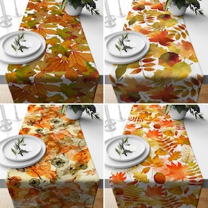 Puede incluir: Cuatro caminos de mesa diferentes con un diseño de hojas de otoño. Los caminos de mesa son blancos con hojas naranjas, amarillas y marrones. Los caminos de mesa miden todos 35,5 cm de ancho y 177,8 cm de largo.