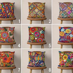 Può includere: Nove fodere per cuscini colorate con vari motivi, tra cui paisley, floreali e geometrici. I cuscini sono disposti in tre file da tre, ogni cuscino appoggiato su una sedia di legno marrone.