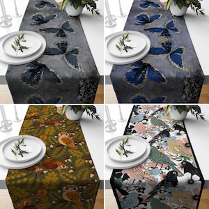 Puede incluir: Cuatro caminos de mesa con diferentes diseños. El primer camino de mesa tiene un fondo gris con un patrón de mariposa plateada. El segundo camino de mesa tiene un fondo gris con un patrón de mariposa azul. El tercer camino de mesa tiene un fondo verde con un patrón de búho marrón. El cuarto camino de mesa tiene un fondo negro con un patrón de pájaro colorido.
