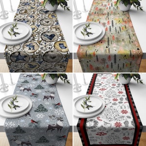 May include: Four different Christmas-themed table runners. The designs include wood slices with festive icons, a forest scene, a winter scene with reindeer, and a black and white holiday sketch with a red border. Each runner is rectangular and placed on a white table.