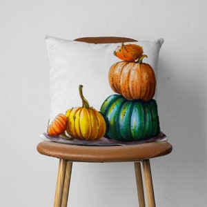 May include: A white throw pillow with a colorful illustration of four pumpkins. The pumpkins are stacked on top of each other and are in shades of orange, yellow, and green.