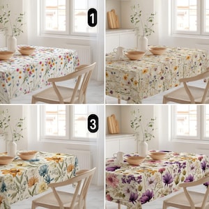 May include: Four floral tablecloths in different color schemes are displayed on tables. Each tablecloth features a repeating pattern of flowers and foliage. The tables are set with wooden bowls, vases, and chairs, creating a cohesive dining setting.