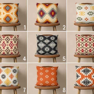 Op de afbeelding: Negen verschillende kussenhoezen met geometrische patronen in verschillende kleuren, waaronder oranje, rood, zwart, wit en geel. De kussens zijn gerangschikt in drie rijen van drie, elk kussen op een houten stoel.
