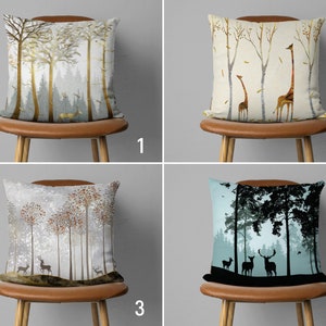 May include: Four throw pillows with different nature-inspired designs. The first pillow features a gold and green forest scene, the second has a beige background with two giraffes, the third has a white background with a snowy forest scene, and the fourth has a blue background with a black silhouette of a forest scene.
