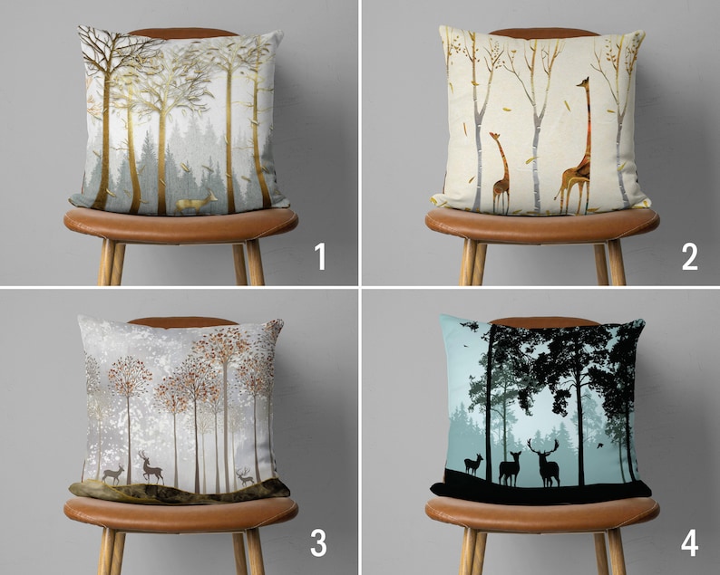 May include: Four throw pillows with different nature-inspired designs. The first pillow features a gold and green forest scene, the second has a beige background with two giraffes, the third has a white background with a snowy forest scene, and the fourth has a blue background with a black silhouette of a forest scene.