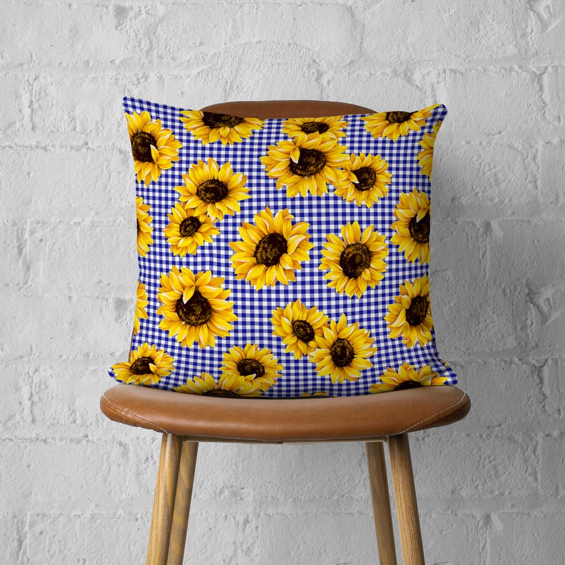 May include: A blue and white gingham pillow with a sunflower pattern. The pillow is made of fabric and has a square shape.
