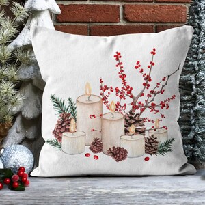 May include: A white throw pillow with a wintery design featuring candles, pine cones, and red berries. The candles are white and have a warm glow. The pine cones are brown and the berries are red.