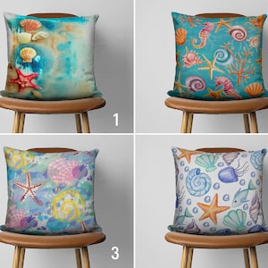 May include: Four decorative throw pillows with different designs featuring seashells, starfish, and other ocean-themed imagery. The pillows are displayed on brown wooden chairs against a white background.