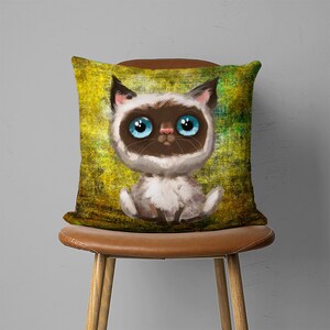 May include: A throw pillow with a cartoon illustration of a Siamese cat with blue eyes on a yellow and green background.