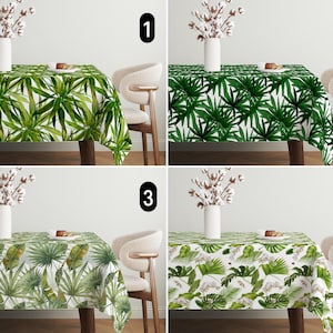 Op de afbeelding: Vier verschillende tafelkleden met een tropisch bladmotief. De tafelkleden zijn wit met groene bladeren. De tafelkleden worden getoond op een tafel met een witte achtergrond. De tafelkleden zijn genummerd van 1 tot en met 4.