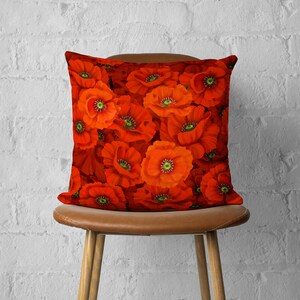 Puede incluir: Una almohada roja con un patr&oacute;n floral de amapolas rojas. La almohada est&aacute; sentada en una silla marr&oacute;n.