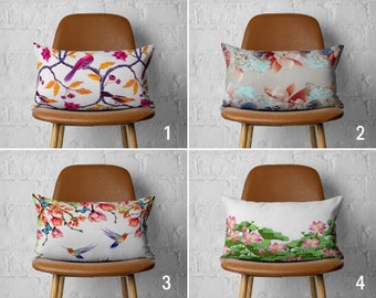 May include: Four throw pillows with different floral and bird designs. The pillows are on brown chairs with wooden legs. The chairs are in front of a white brick wall.