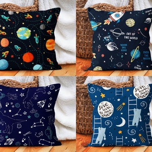 Op de afbeelding: Vier verschillende blauwe en witte kussens met ruimtethema's. De kussens hebben planeten, sterren, raketten en andere ruimte-afbeeldingen. De tekst op de kussens is "Space Fun", "Out of this World", "Over the Moon" en "Love you to the moon".