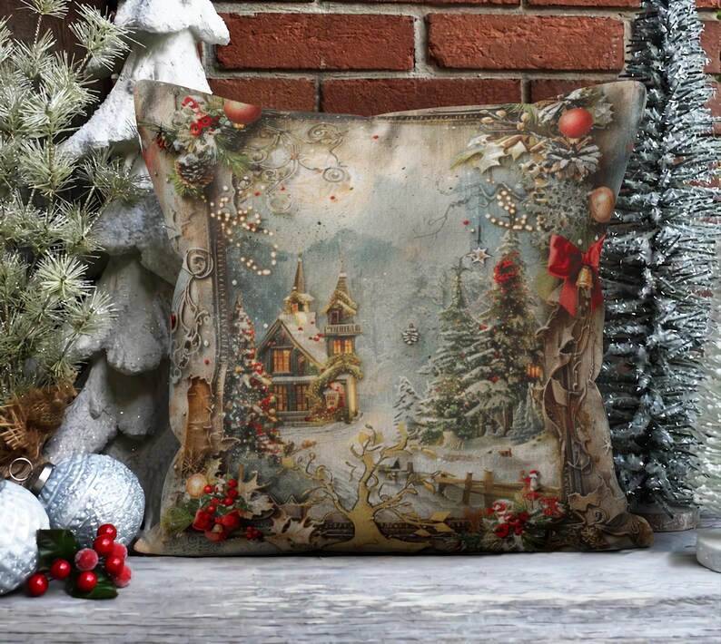 May include: A decorative throw pillow with a vintage Christmas scene featuring a snowy village with a church, trees, and a red ribbon. The pillow has a beige background with a brown border.