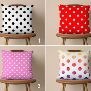 Könnte beinhalten: Vier dekorative Kissen mit Polka-Dot-Mustern. Die Kissen zeigen schwarze Punkte auf Weiß, weiße Punkte auf Rot, weiße Punkte auf Rosa und mehrfarbige Punkte auf Weiß. Jedes Kissen wird auf einem Holzschemel präsentiert.