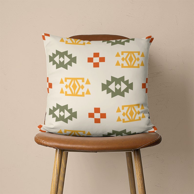Op de afbeelding: Een wit kussen met een geometrisch patroon in tinten groen, geel, oranje en rood. Het patroon bevat herhalende vierkanten en driehoeken.
