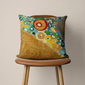 Puede incluir: Una almohada decorativa con un dise&ntilde;o abstracto colorido que presenta c&iacute;rculos y remolinos en tonos de azul, amarillo, verde, rojo y dorado. La almohada est&aacute; sobre una silla marr&oacute;n.