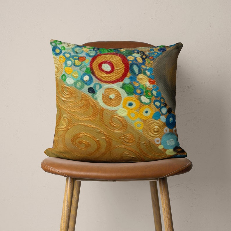 Puede incluir: Una almohada decorativa con un dise&ntilde;o abstracto colorido que presenta c&iacute;rculos y remolinos en tonos de azul, amarillo, verde, rojo y dorado. La almohada est&aacute; sobre una silla marr&oacute;n.