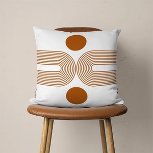Pu&ograve; includere: Cuscino bianco con un design geometrico con due cerchi marroni e due set di archi marroni.