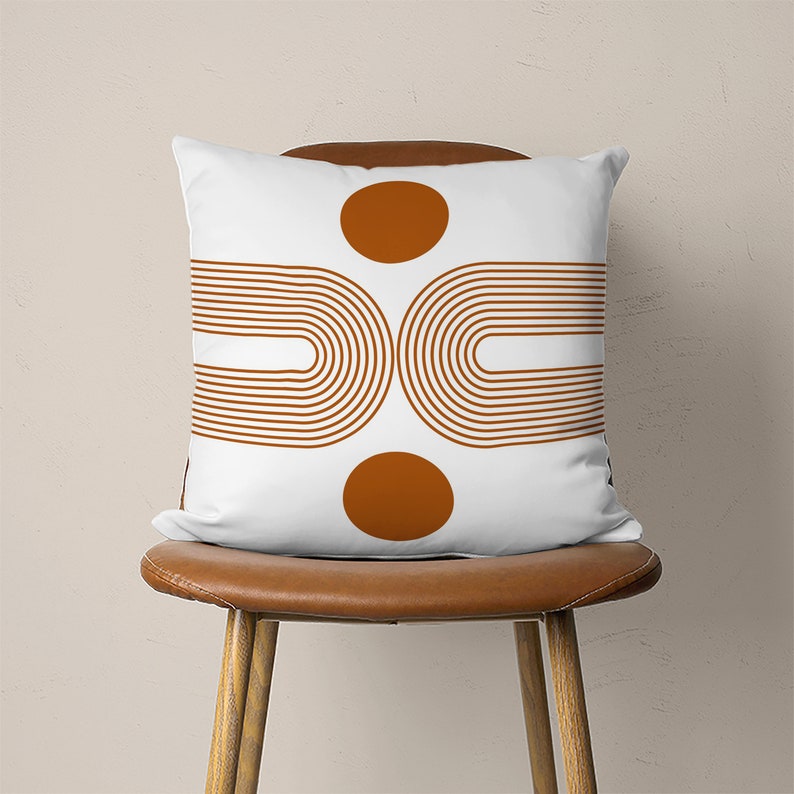 Pu&ograve; includere: Cuscino bianco con un design geometrico con due cerchi marroni e due set di archi marroni.