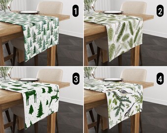 May include: Four different table runners with various winter-themed patterns. The first runner features a green and white pattern of pine trees. The second runner has a green and white pattern of pine branches. The third runner has a white background with green pine trees and deer. The fourth runner has a white background with green pine branches and birds.