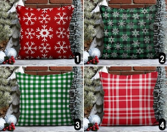 May include: Four different Christmas themed throw pillow covers. The first pillow cover is red with white snowflakes. The second pillow cover is green with white snowflakes on a black and white plaid background. The third pillow cover is green and white plaid. The fourth pillow cover is red and white plaid.