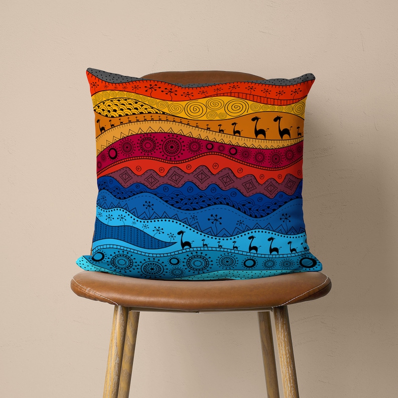 Op de afbeelding: Een kleurrijk kussen met een geometrisch patroon met golvende lijnen, cirkels en gestileerde dierfiguren. Het kussen is in tinten rood, oranje, geel, blauw en groen.