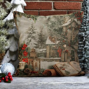 May include: A decorative throw pillow with a winter scene featuring a snow-covered house, trees, and a lantern. The pillow has a beige background with red berries and a vintage book.
