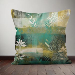 Op de afbeelding: Een groen en gouden kussen met een aquarel-achtig bloemenpatroon. Het kussen heeft verschillende bladontwerpen in tinten groen, goud en wit.