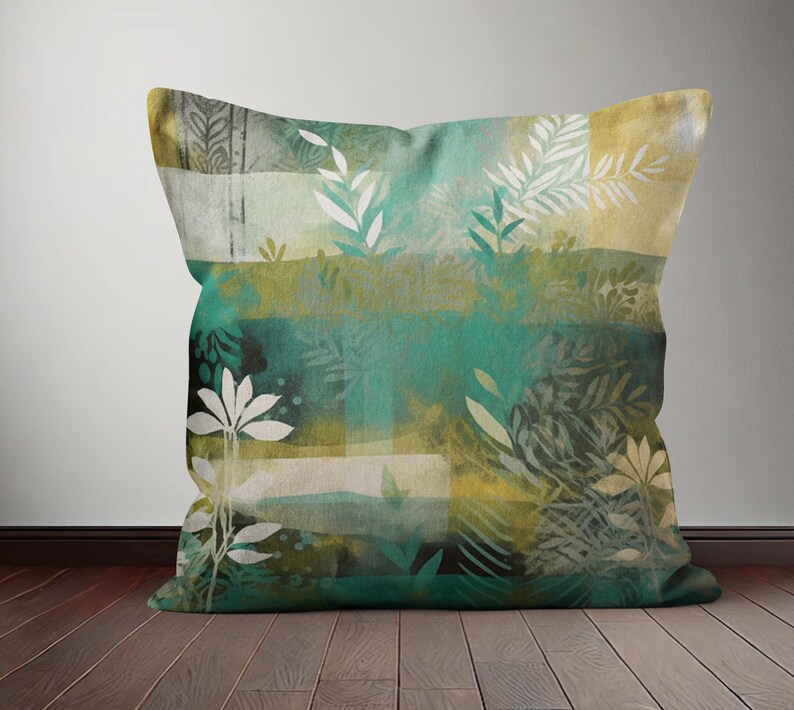 Op de afbeelding: Een groen en gouden kussen met een aquarel-achtig bloemenpatroon. Het kussen heeft verschillende bladontwerpen in tinten groen, goud en wit.
