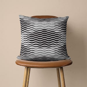 May include: A black and white wavy patterned throw pillow on a brown leather chair.