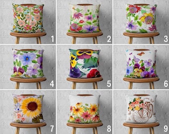 May include: Nine decorative throw pillows with floral designs, each on a wooden stool. The pillows feature various watercolor flower patterns, including sunflowers, pansies, and mixed blooms in vibrant colors like pink, yellow, purple, and red. The pillows are square-shaped.