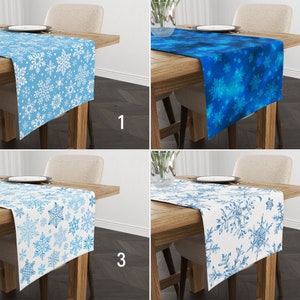 May include: Four table runners with snowflake patterns. The runners are in blue and white, with different designs. The runners are on wooden tables with chairs.