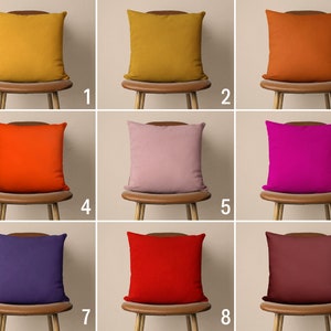 Op de afbeelding: Negen verschillende gekleurde kussens op houten stoelen. De kussens zijn in de volgende kleuren: mosterdgeel, oranje, roze, magenta, paars, rood, bruin.