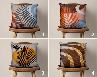 May include: Four throw pillows with abstract designs featuring stylized leaves in various colors, including orange, yellow, blue, and brown. The pillows are displayed on brown chairs with wooden legs.