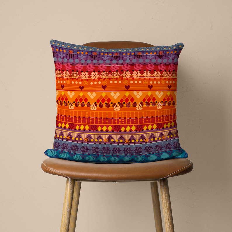 Op de afbeelding: Een kleurrijk kussen met een geometrisch patroon in tinten oranje, rood, paars en blauw. Het kussen ligt op een bruine leren stoel.