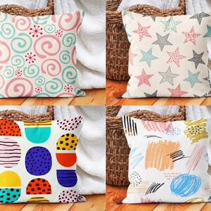 May include: Four decorative throw pillows with different patterns. The pillows are white with colourful geometric designs. The designs include swirls, stars, circles, and abstract lines.