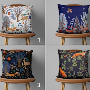 Puede incluir: Cuatro cojines decorativos con diferentes patrones de tem&aacute;tica forestal. Los cojines presentan zorros, ciervos y &aacute;rboles en tonos de azul, verde, rojo y blanco. Los cojines se muestran en sillas marrones sobre un fondo blanco.
