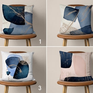 May include: Four throw pillows with abstract designs in shades of blue, gold, and pink. The pillows are on brown chairs with wooden legs.